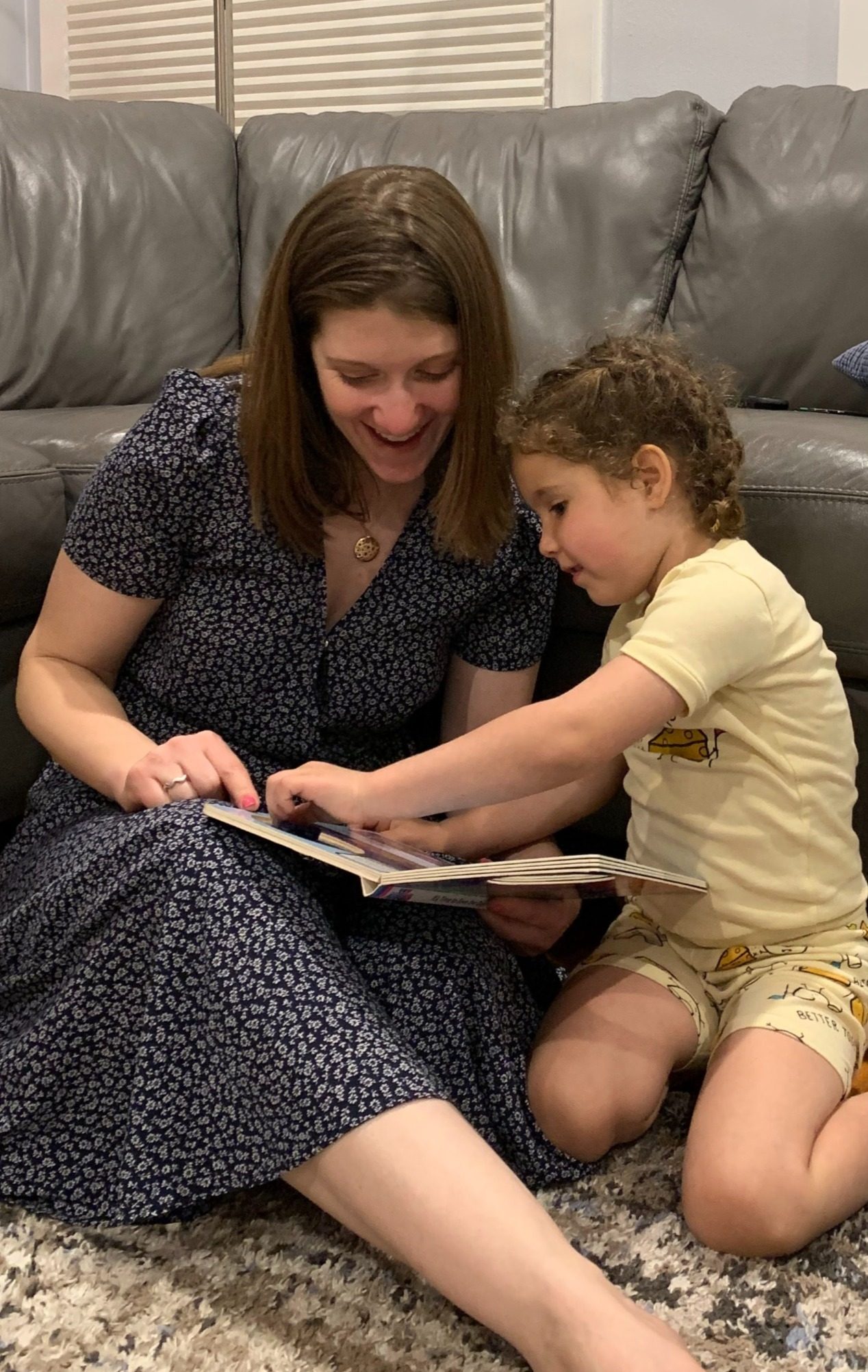 Devra reading a picture book on the floor with a young child.