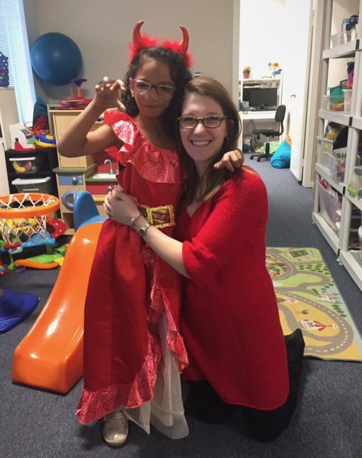 Devra and a young client in costume, smiling together in a therapy room.